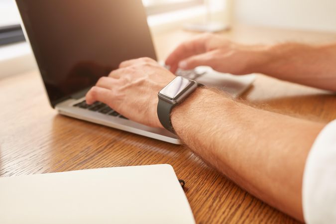 Close up image of man with a smartwatch working on laptop