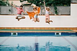 two young women and a man jumping by the pool