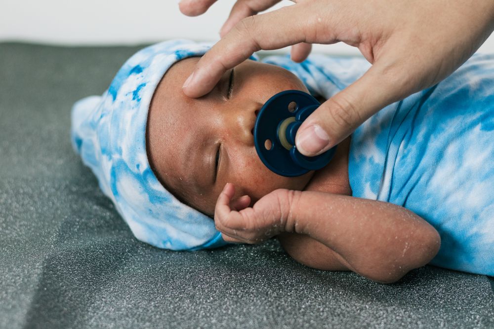 Anonymous mother with newborn baby wrapped on soft blanket with pacifier