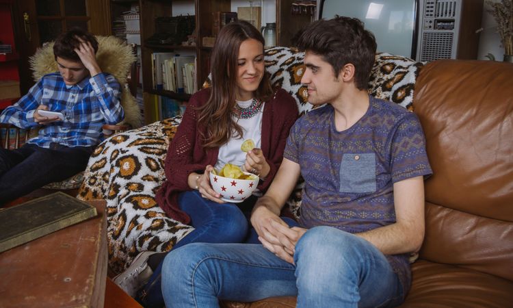 Couple eating chips on a sofa and friend looking smartphone