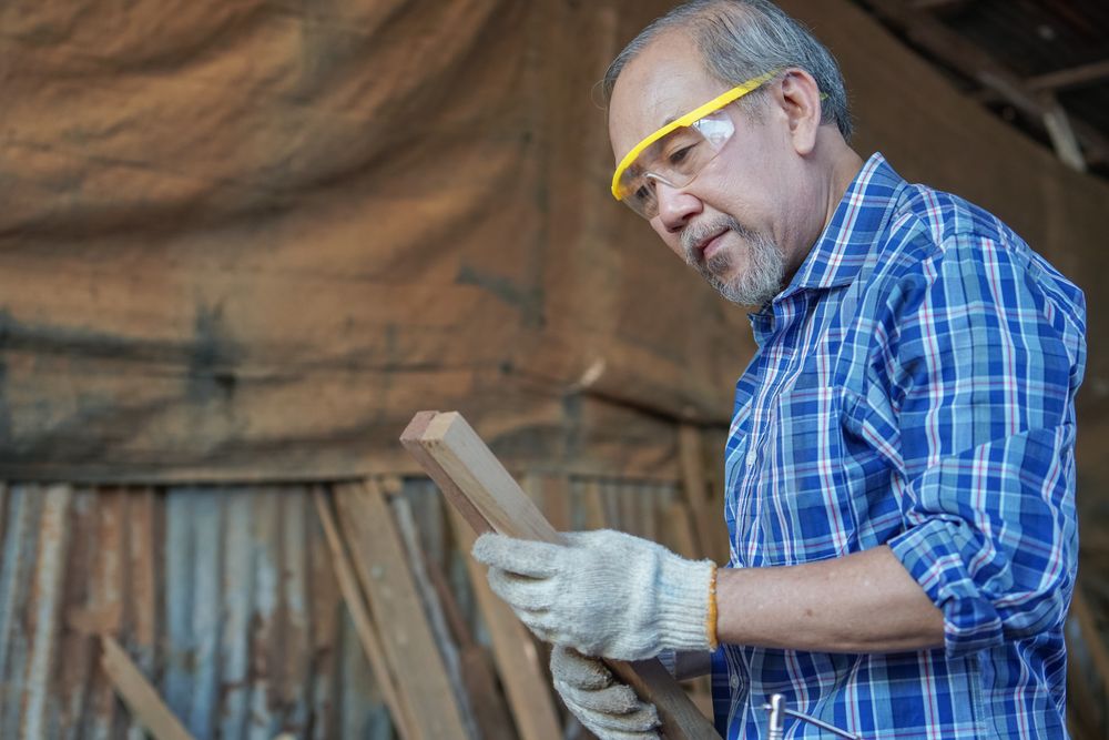 Asian male woodworker picks a wooden panel to work with in shop