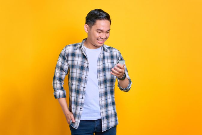 Very happy Asian male looking down at his phone in studio shoot with copy space