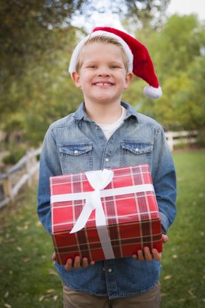Young Boy Wearing Holiday Clothing Holding Christmas Gift Outside