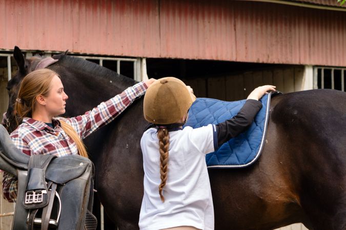 Instructor assisting girl to place saddle pad on horse