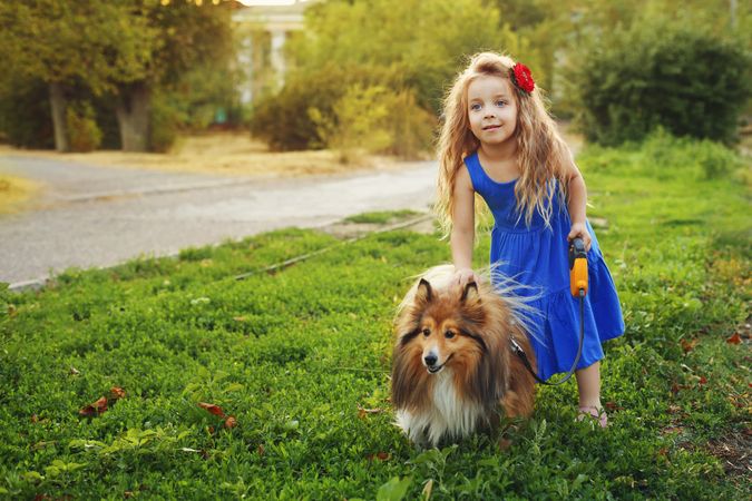 Girl in blue dress playing with pet dog in the grass