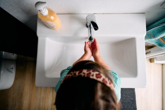 A little brunette girl with a green baby is washing her hands in
