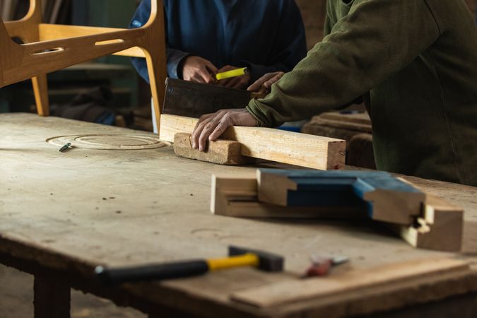 Joiner cutting wood with colleague measuring height