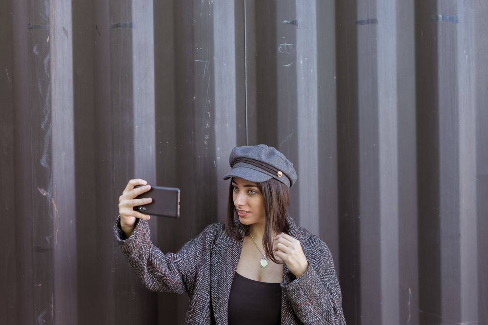 Charming Hispanic lady taking selfie near wall