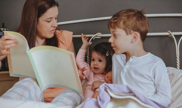 Portrait of mother reading book to her daughter and son in bed