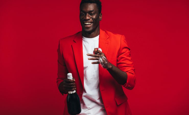 Cheerful young Black man with champagne bottle and glass