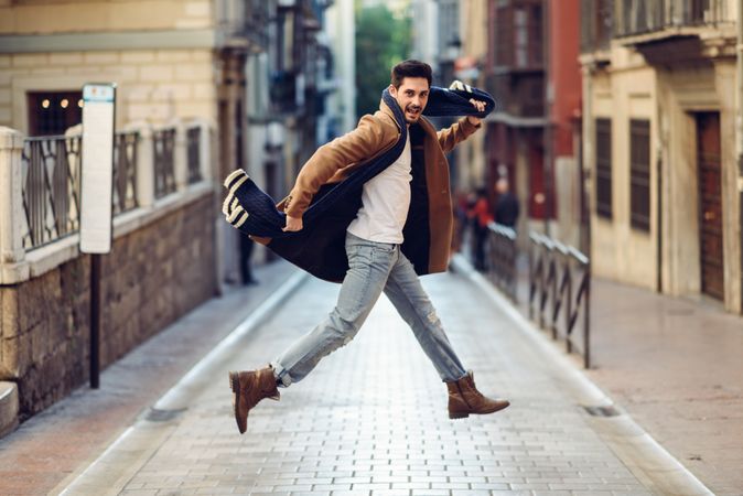 Man in scarf having fun while leaping in center of street