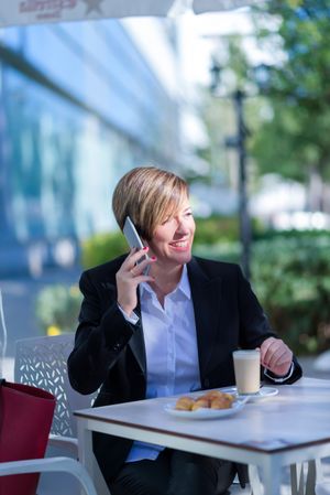 Business woman sitting outside with coffee and cell phone