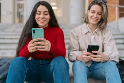 two students sitting on the stairs watching the mobile