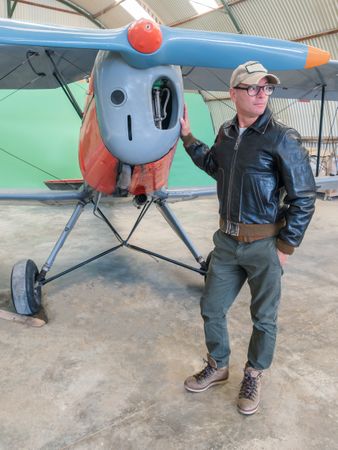 Confident pilot beside retro plane in hangar