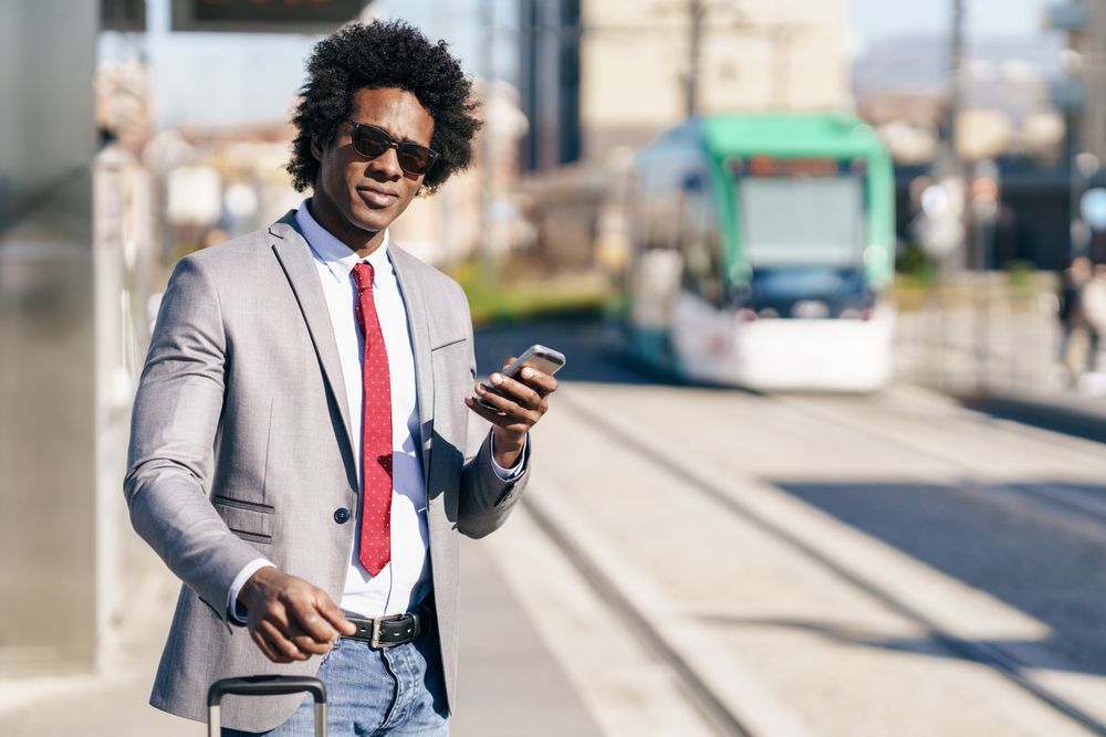 Man in jeans and dress shirt with tie looking up from phone at train station