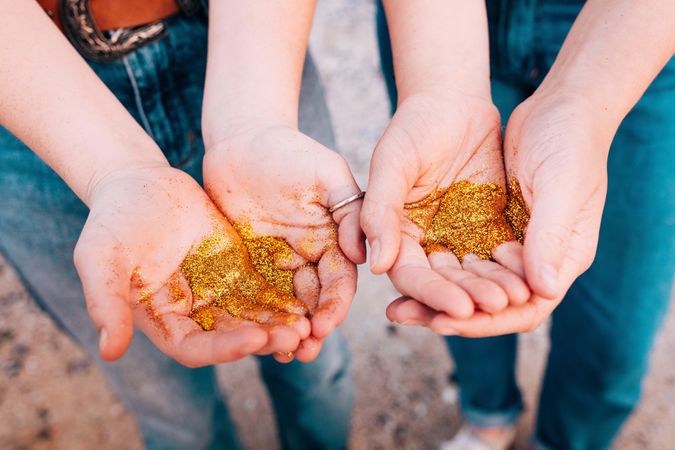 Two sets of young women’s hands holding gold glitter