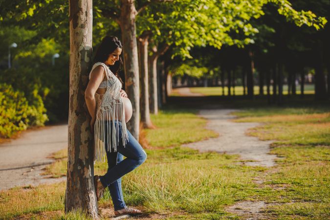 Pregnant female leaning on tree in park
