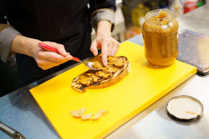 Hands plating spread on a piece of toast in professional kitchen