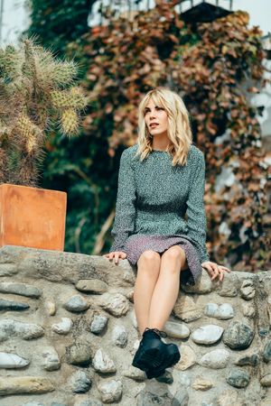 Blonde female with floral dress calmly sitting on stone wall