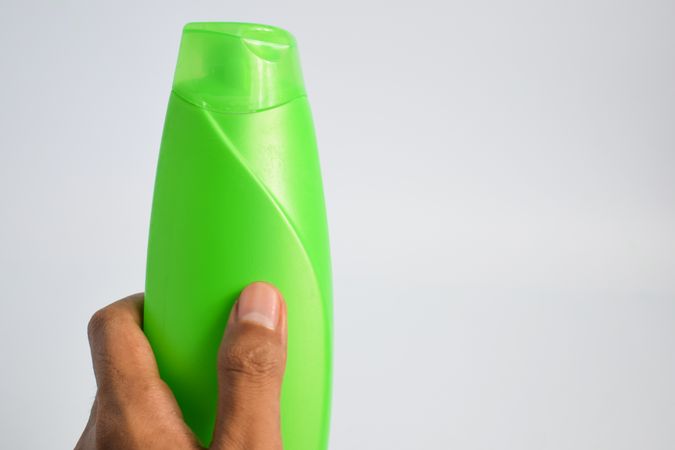 Hand holding blank green shampoo bottle