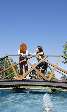 Woman in a wheelchair and female friend on bridge, vertical