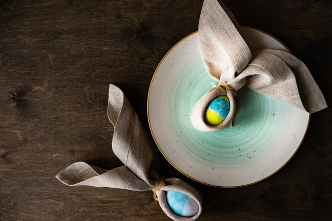 Easter eggs wrapped with rabbit ears with napkin with ceramic plate on wooden table