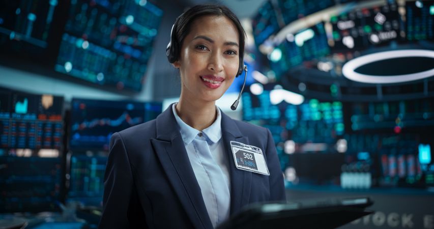 Portrait of a Asian Female Working in an International Stock Exchange Hall: Happy Specialist Wearing Headphones and Using Tablet Computer