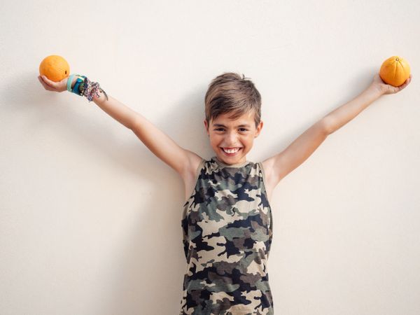 Laughing boy raising hands with oranges up