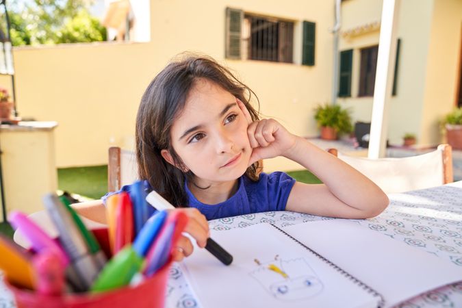 Little girl thinking while drawing on paper