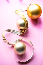 Gold Christmas baubles on pink background with ribbon