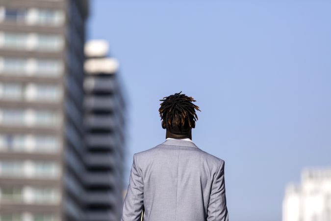 Back of Black man in elegant suit walking on the street against a blue sky