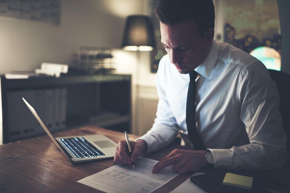 Man in shirt and tie working on documents late at night at his desk