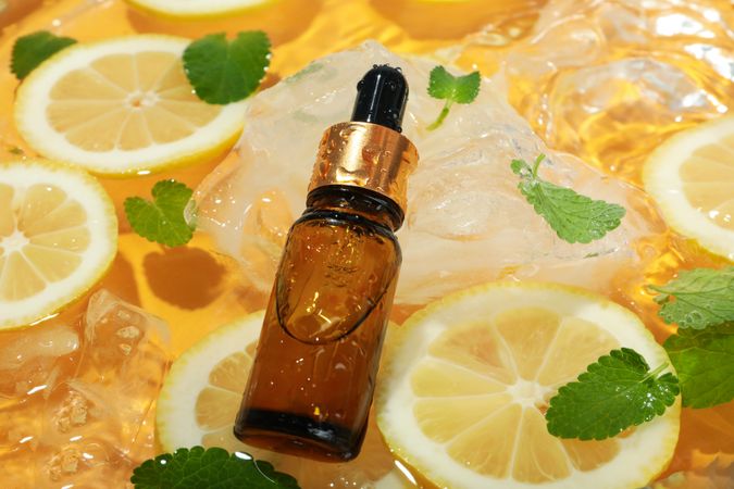 Lemon slices floating in water with mint slices, ice and cosmetic bottle with dropper