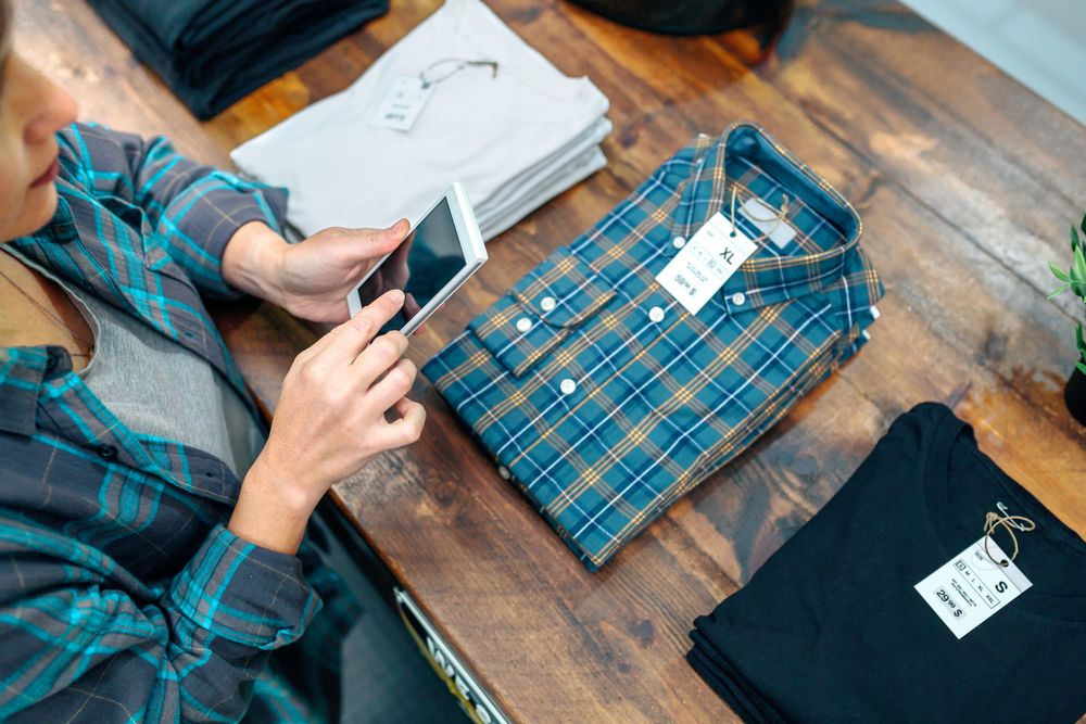Top view of young female customer taking photo of plaid shirt over counter in clothes shop