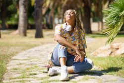 Female sitting on skateboard walkway in park enjoying the sun