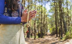Close up of clasping hands holding a japa mala.  Copy space