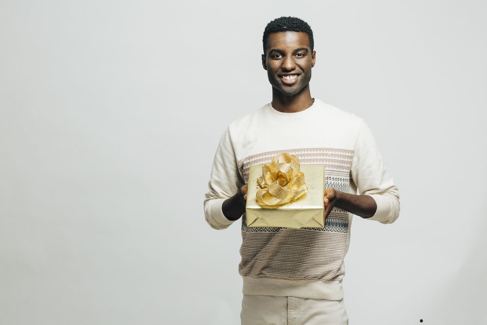 Smiling Black man presenting a gift wrapped in gold paper