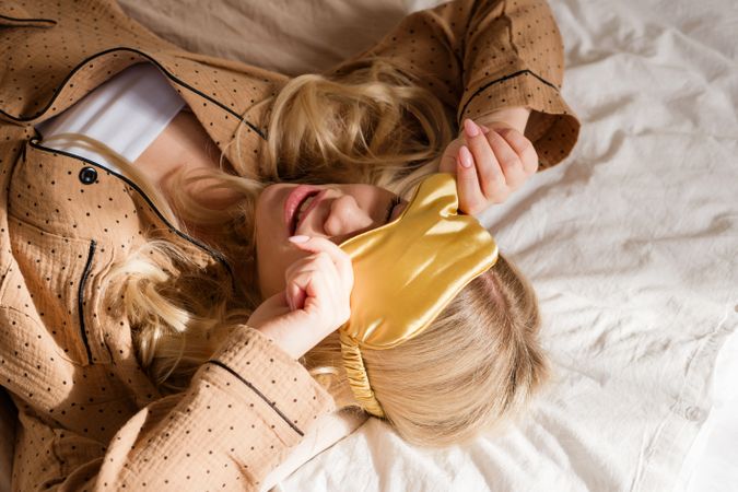 Smiling woman lying on bed, covering eyes with headband.
