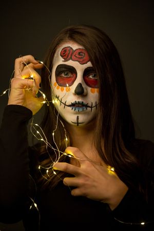 Young woman with creepy face paint holding fairy lights
