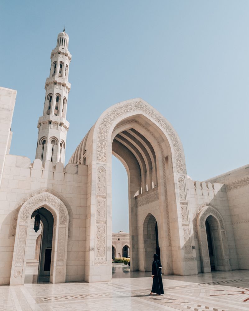 Woman in dark thobe walking beside Sultan Qaboos Grand Mosque in Muscat, Oman