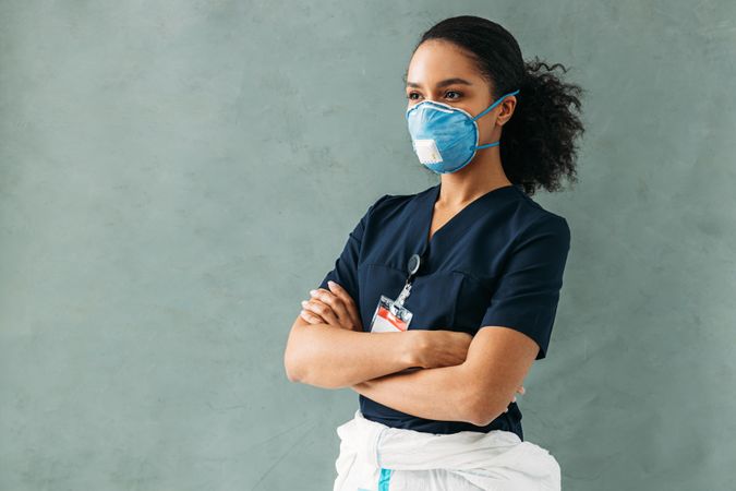 Side view of female medical professional in protective mask with arms crossed