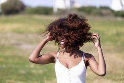 Female pictured outside in park playing with her curly hair in the wind