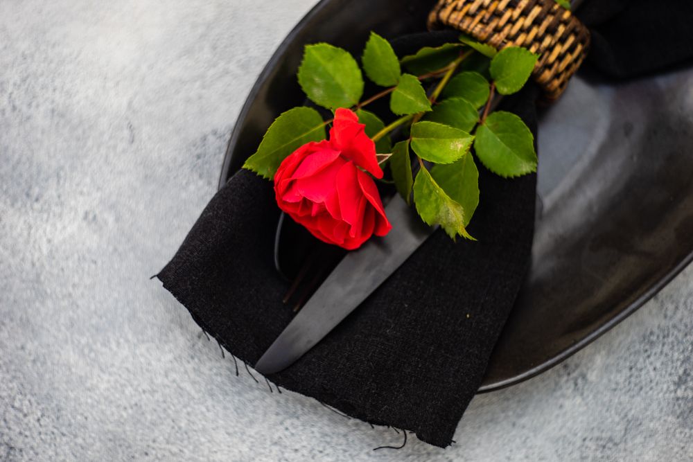 Top view of table setting with red rose on dark plate