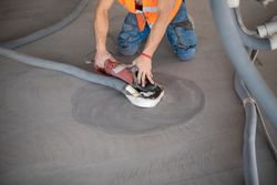 Worker working on the floor of an industrial building. Construction worker producing grout and finishing wet concrete floor.