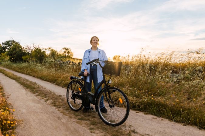 blonde woman standing with a bike in a field at sunset