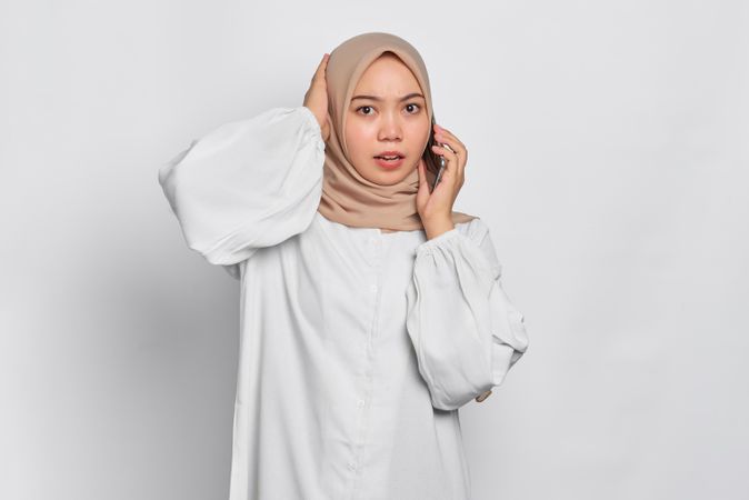 Confused Asian Muslim woman talking on cell phone