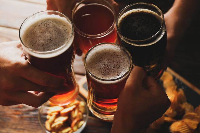 Four men cheers with beer on wooden background with snacks