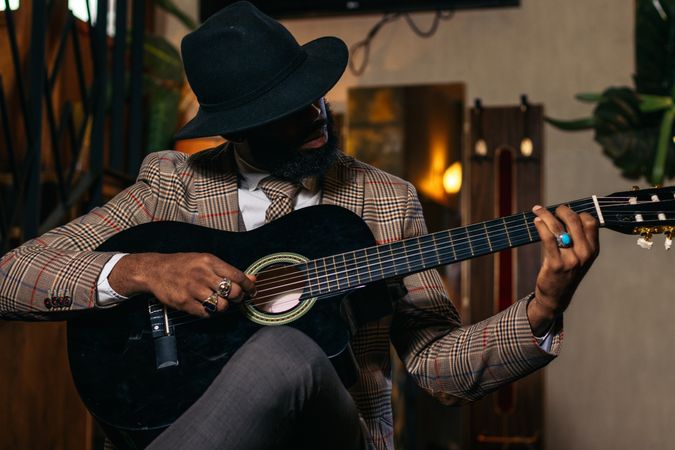Stylish Black man in classic outfit playing guitar