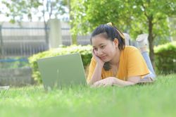 A young woman lying on the lawn at home using a laptop.