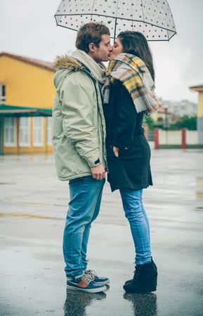 Side view of couple kissing under dotted umbrella on rainy day